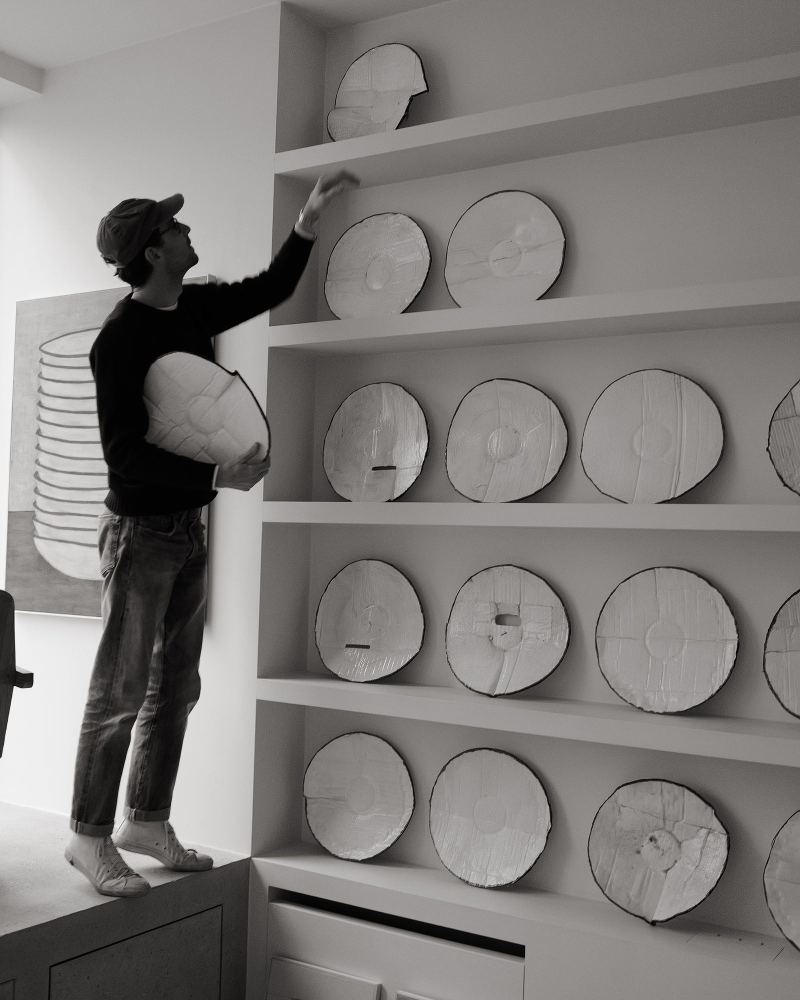Person arranging circular objects on a shelf in a minimalistic room.