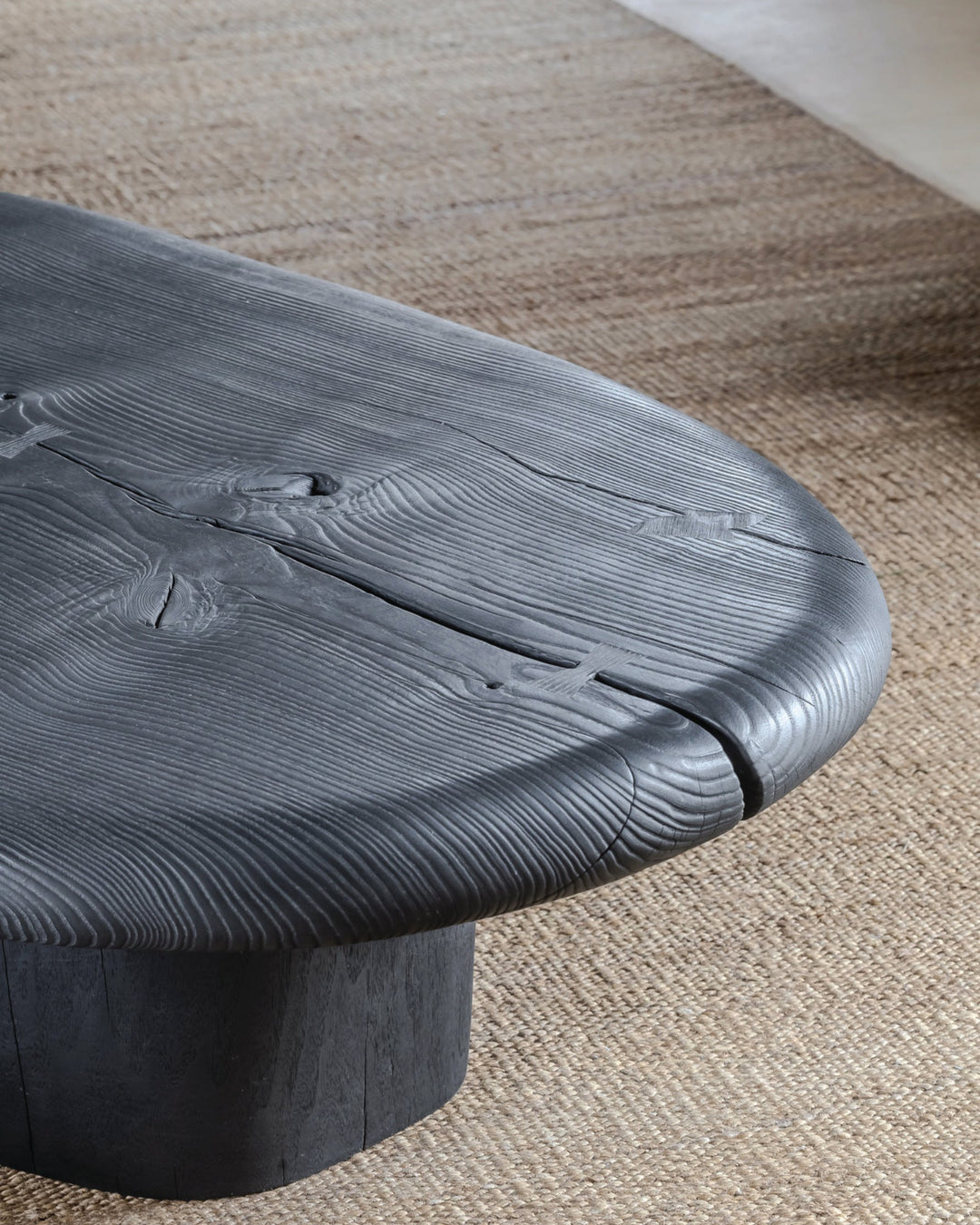 A close-up of a black, textured coffee table with a unique design, placed on a beige carpet.