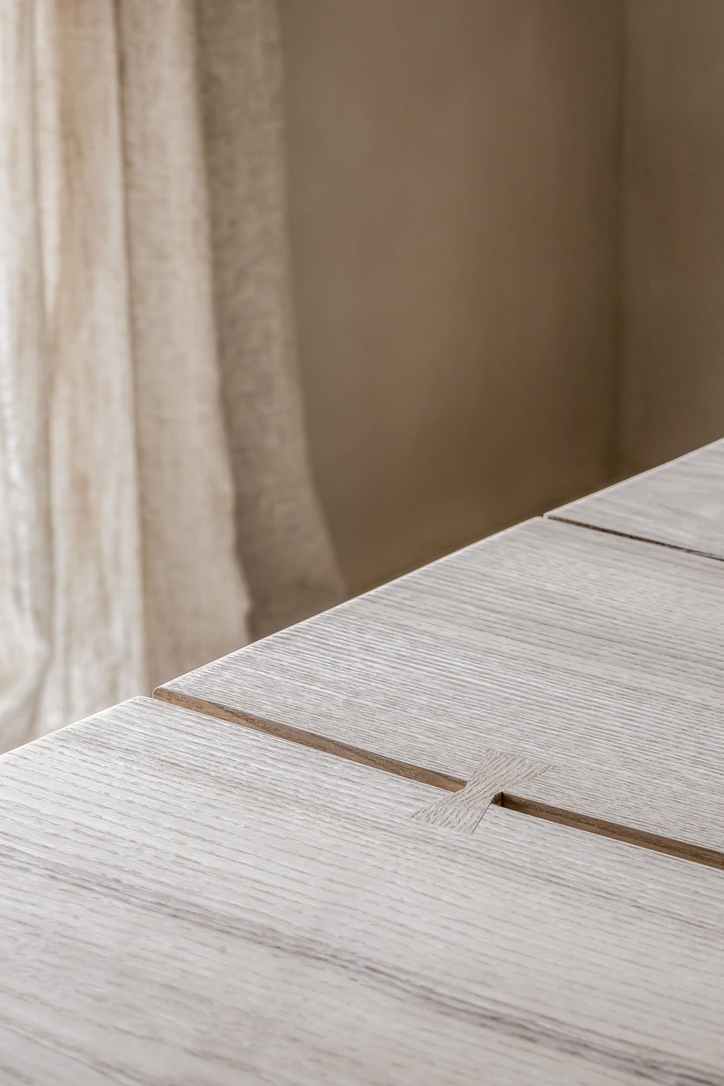 Close-up of a wooden surface with a subtle pattern, blurred curtain in the background