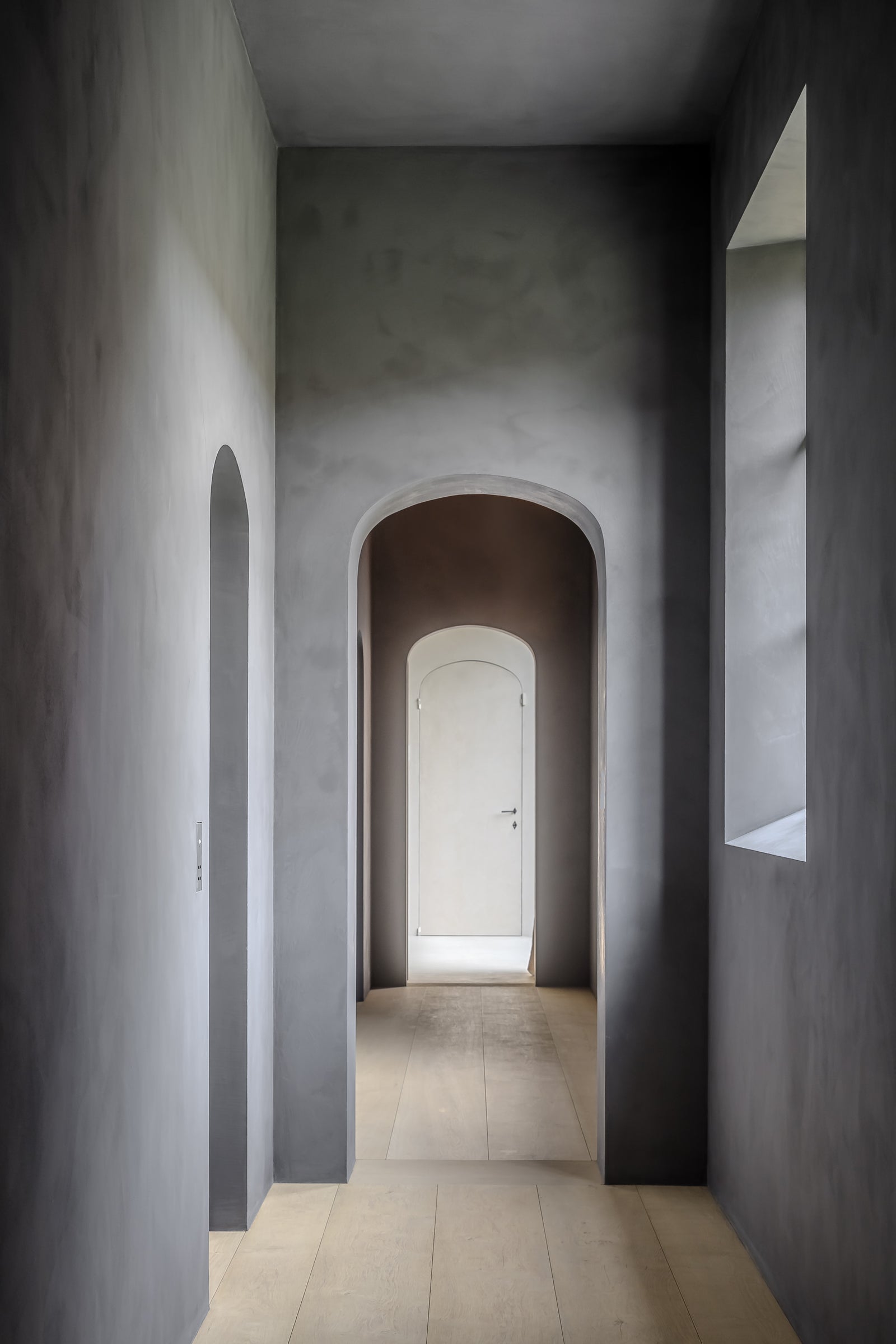 Long, narrow hallway with arched doorways and a light at the end.
