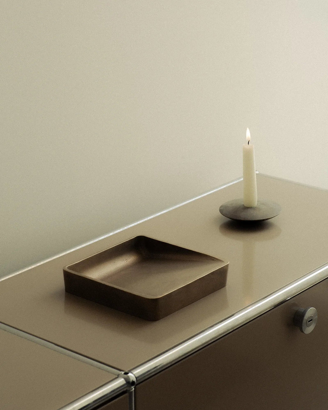 Brown rectangular tray and candle on a reflective surface with a neutral background